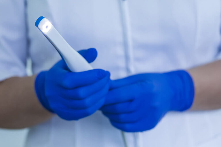 Dental professional wearing blue gloves and holding an intraoral camera.