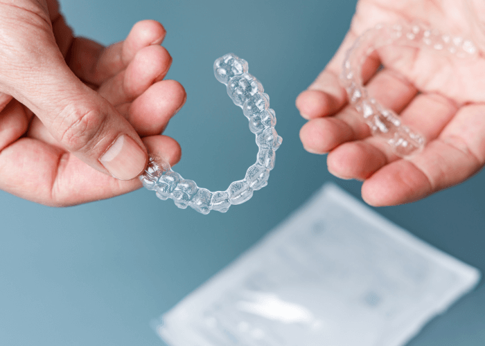 Close-up image of a pair of hands holding clear Invisalign aligners.